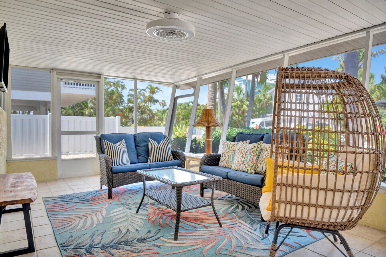 A sunroom with a blue sofa, a wicker chair, and a patterned rug.