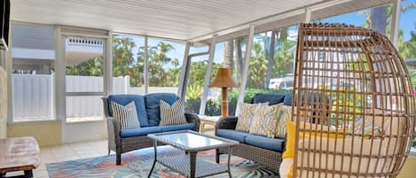 A sunroom with a blue sofa, a wicker chair, and a patterned rug.