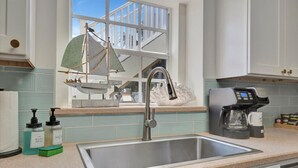 Une cuisine équipée d’un évier en acier inoxydable, d’une machine à café et d’une voile décorative suspendue près de la fenêtre.