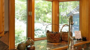A corner with large windows, a basket with pinecones, a soap dispenser, and a sign on the windowsill.