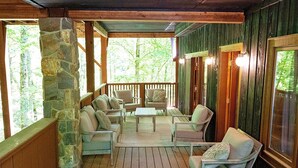 A covered porch with stone walls, wooden beams, and a seating area with chairs and a table.