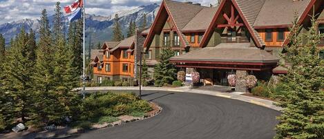 A lodge with a prominent red and brown wooden structure, surrounded by pine trees and a mountain backdrop.