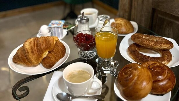 Una tavola imbandita per la colazione con croissant, pasticcini, un bicchiere di succo d'arancia, una tazza di caffè e condimenti.