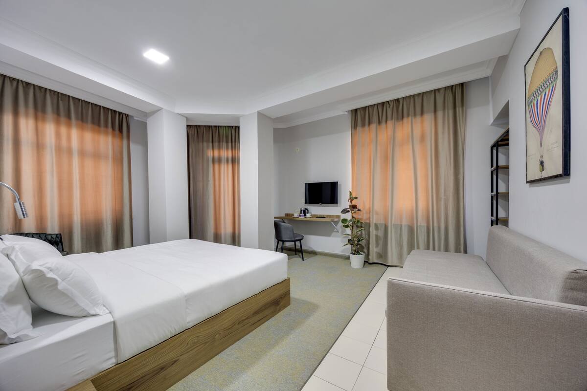 A hotel room with a bed, a desk, a chair, a sofa, and a television.