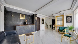 Un'area reception di un hotel con una scrivania neri e due divani: uno in pelle nera e uno verde.