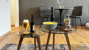 Uma sala de estar moderna com uma mesa de centro de vidro, duas cadeiras, uma televisão fixada numa parede listrada e um recipiente com lanches.