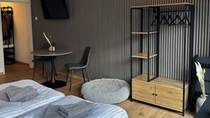 Quarto de hotel moderno com duas camas, uma escrivaninha, uma cadeira, uma televisão e um guarda-roupa.