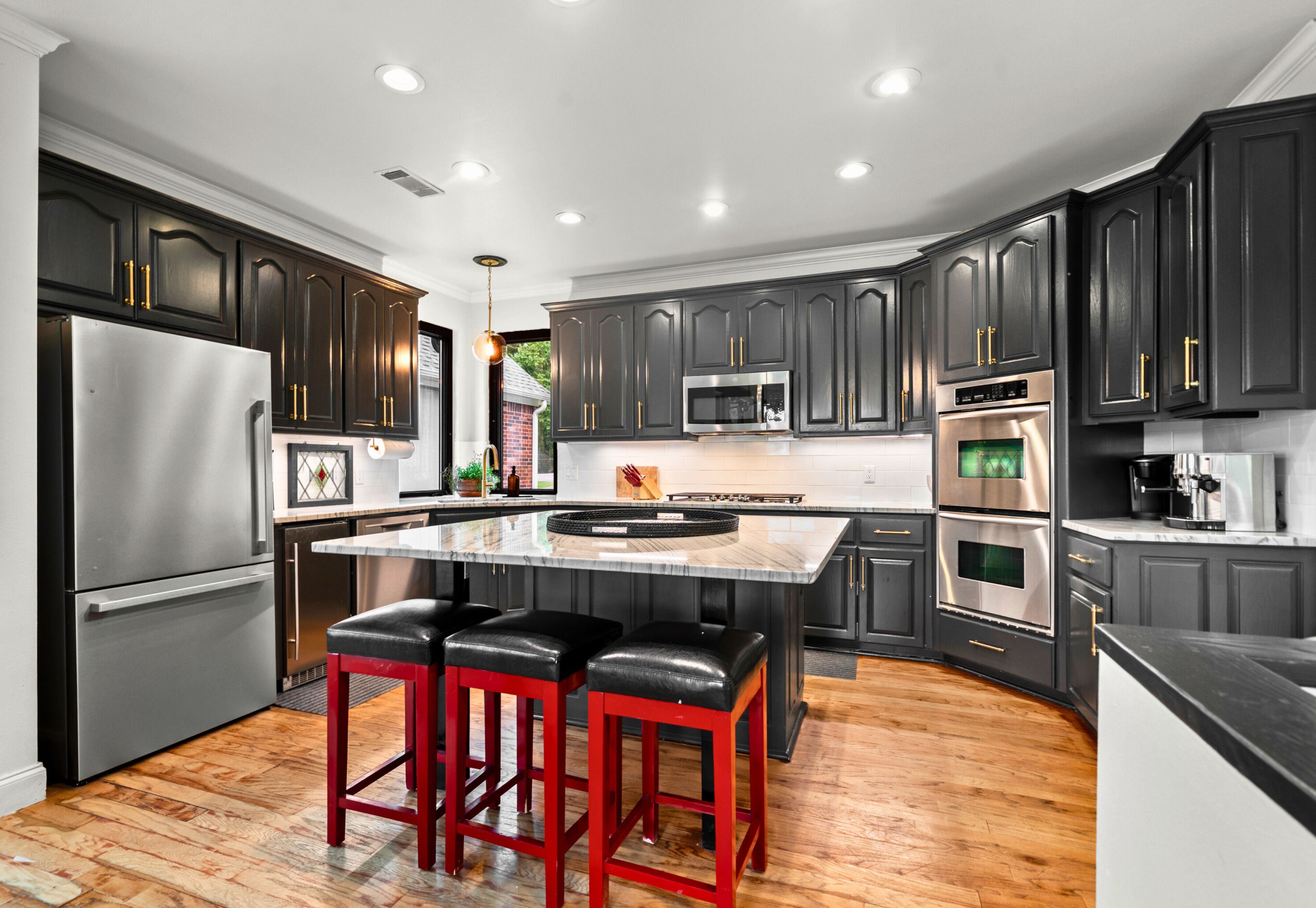 Une cuisine moderne avec des meubles de couleur sombre, des appareils en acier inoxydable, un îlot central doté de tabourets et un plancher en bois.