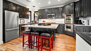 A modern kitchen with dark cabinets, stainless steel appliances, a central island with stools, and a wooden floor. - Lakefront Luxury w/Private Heated Pool & Dock (Hot Springs)