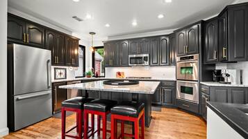 Une cuisine moderne avec des meubles de couleur sombre, des appareils en acier inoxydable, un îlot central doté de tabourets et un plancher en bois.