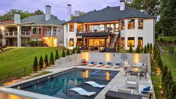 Une grande maison avec une piscine, un espace extérieur aménagé pour s’asseoir et une terrasse bien éclairée.