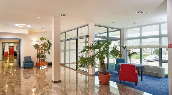 A spacious lobby with a polished marble floor, large windows offering views of the street, and several potted plants. - HOTEL EUROPA (Karlovac)