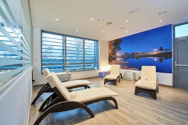 Una habitación con dos sillones, un ventanal con persianas, un mural en la pared y una mesa con lámpara.
