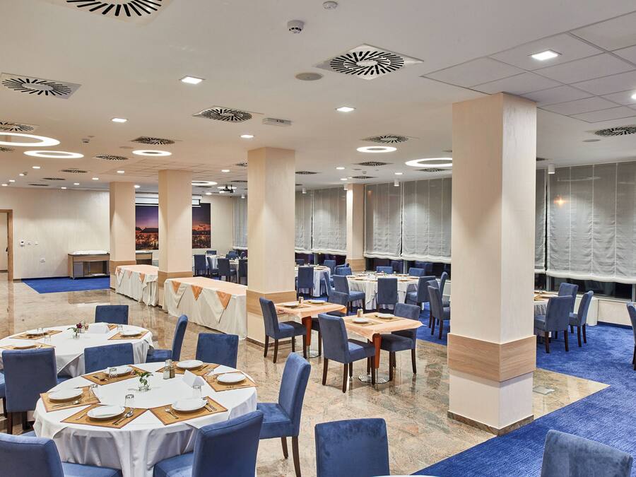 Una vasta sala da banchetti con tavoli rotondi, sedie blu e un tappeto azzurro.