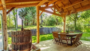 Een houten terras met een rustieke vuurkuil, buitenmeubels en uitzicht op een weelderige tuin.