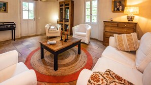 Een knusse woonkamer met een houten plafond, witte banken, een bijzettafeltje en een open haard.