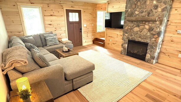 Una sala de estar acogedora con chimenea de piedra, paredes de madera y un amplio sofá modular.