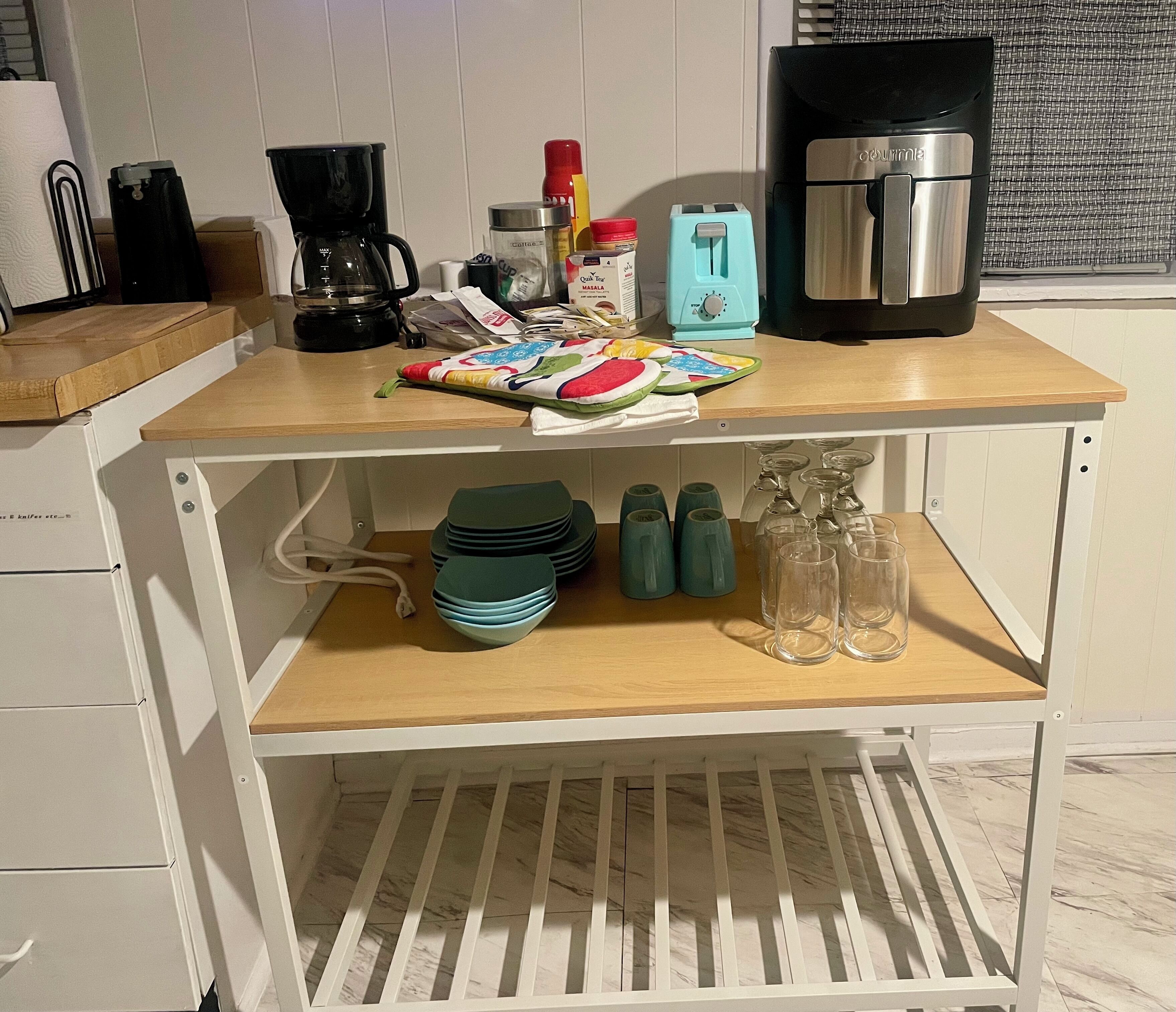 Uma bancada de cozinha com uma cafeteira, uma torradeira e um liquidificador. Também há pratos verdes, um pote de geleia e uma garrafa de leite na bancada.