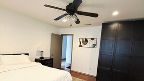 A bedroom with a bed, a ceiling fan, a nightstand, a door, and a wardrobe.