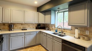 A modern kitchen with white cabinets, a built-in dishwasher, and a window with a view of greenery.