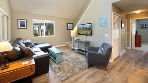 Una sala de estar con sofá, sillón y televisor sobre un mueble.