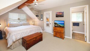 Un dormitorio con una cama, un cofre de madera, un televisor y un ventilador de techo.