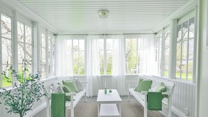 A bright, white-paneled room with a large window, a white table, and two green-cushioned chairs. - In the eastern wing, 6 people accommodate in a three two-person rooms (Unknown)