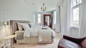 A bedroom with a large bed, a wooden chair, a mirror, and a chandelier. - In the eastern wing, 6 people accommodate in a three two-person rooms (Unknown)