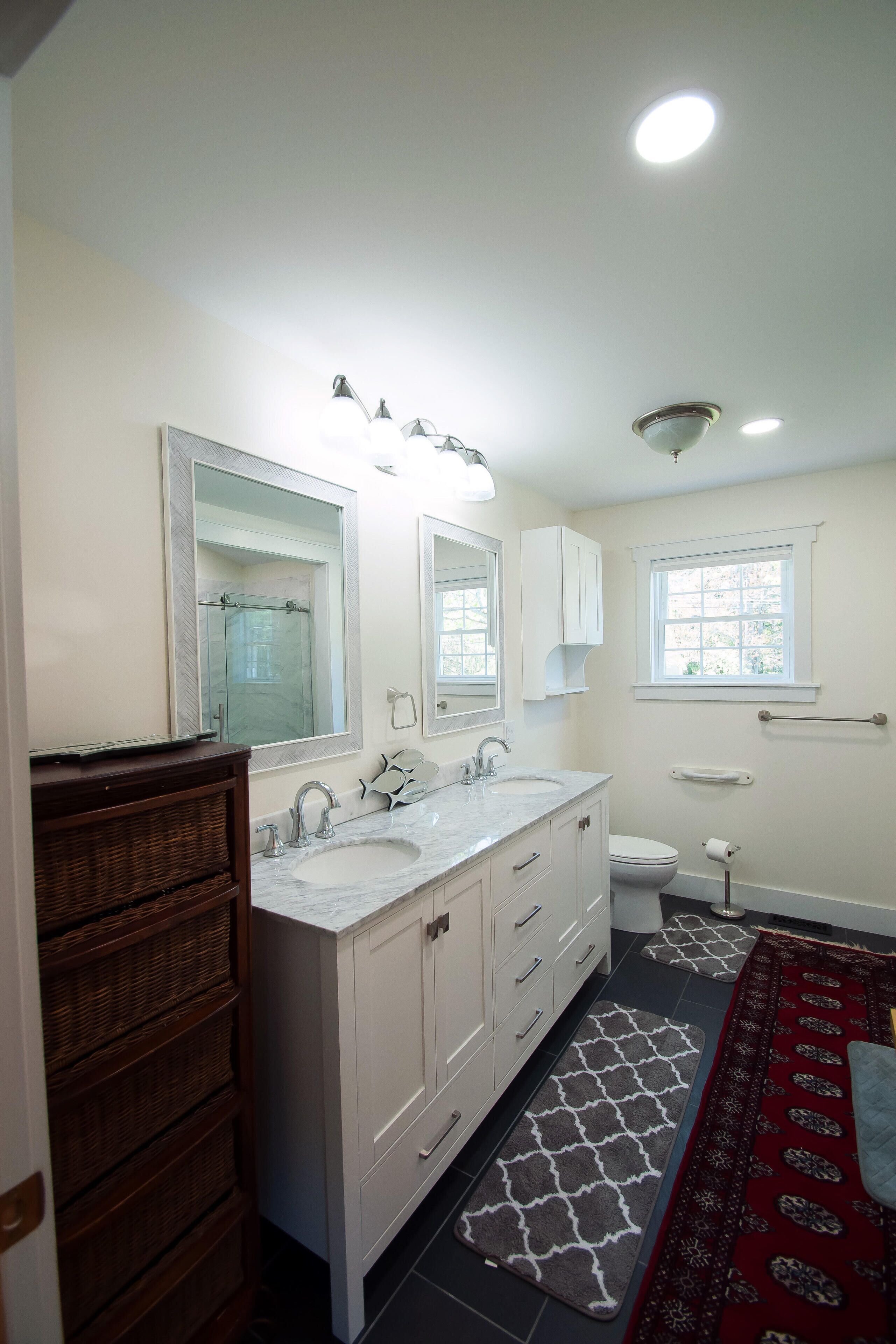 A bathroom with a double sink vanity, a toilet, a window, and a mirror.