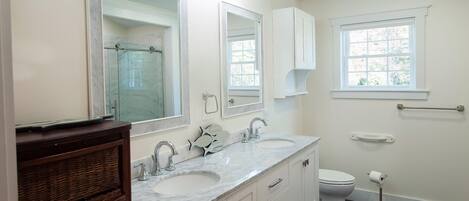 A bathroom with a double sink vanity, a toilet, a window, and a mirror.