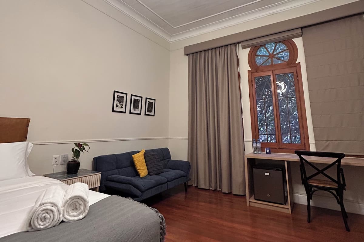A hotel room with a bed, a sofa, a desk, and a window with curtains.