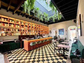 Un bar au sol à carreaux, avec des étagères remplies de bouteilles et des plantes suspendues.