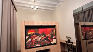A room with a wooden TV stand, a ceiling with exposed beams, a chandelier, a desk with a chair, and a potted plant. - Andara Hotel (Lima)