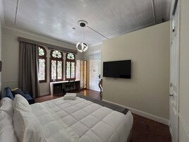 Une chambre à coucher avec un grand lit, un bureau, une télévision et une fenêtre avec des rideaux.