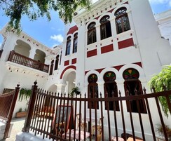Un bâtiment blanc agrémenté de touches de rouge, avec des fenêtres en arc de cercle et des balcons.