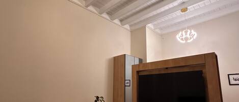 A hotel room with a bed, a desk, a chair, a TV, and a ceiling light.