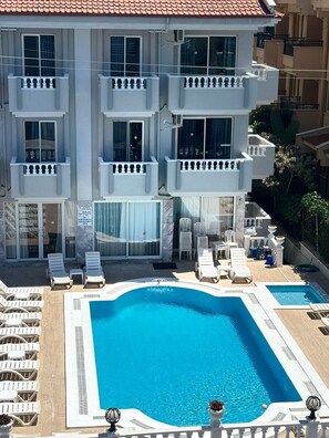 A multi-story hotel with a swimming pool, outdoor seating, and a view of neighboring buildings. - Basak Apart (Marmaris)