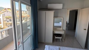 Habitació d'hotel amb balcó, un llit, escriptori, armari i aire condicionat.