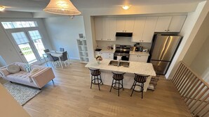 Cozinha moderna com ilha central, eletrodomésticos de aço inoxidável e área de refeições com sofá e cadeiras.