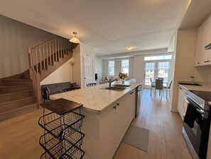 A modern kitchen with a marble countertop, wooden staircase, and a view to the living area.