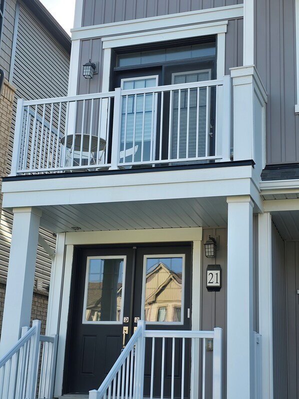 A two-story building with a black front door, white railings, and a balcony with a black railing.