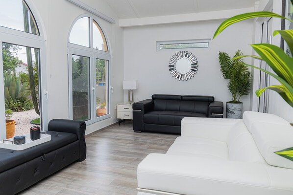 A modern living room with a black and white sofa set, a white sofa, and a large window with a view of greenery.