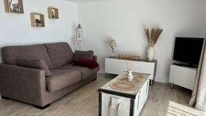 Una sala moderna con un sofá marrón, una consola blanca, una mesa de centro de estilo rústico, un televisor y una lámpara.