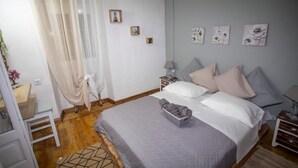 A bedroom with a bed, bedside tables, a nightstand, a lamp, and a window with a curtain. - Archontissa Sea View House (Mesongi)