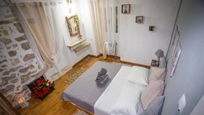 A bedroom with a wooden floor, a bed with white linens, a small bedside table, a mirror, and a wall-mounted shelf. - Archontissa Sea View House (Mesongi)