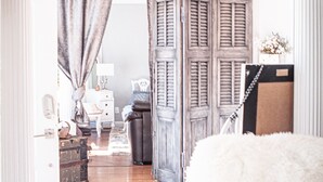 Una habitación con una araña de cristal, una puerta de madera con contraventanas, un aparador blanco y una alfombra mullida blanca.