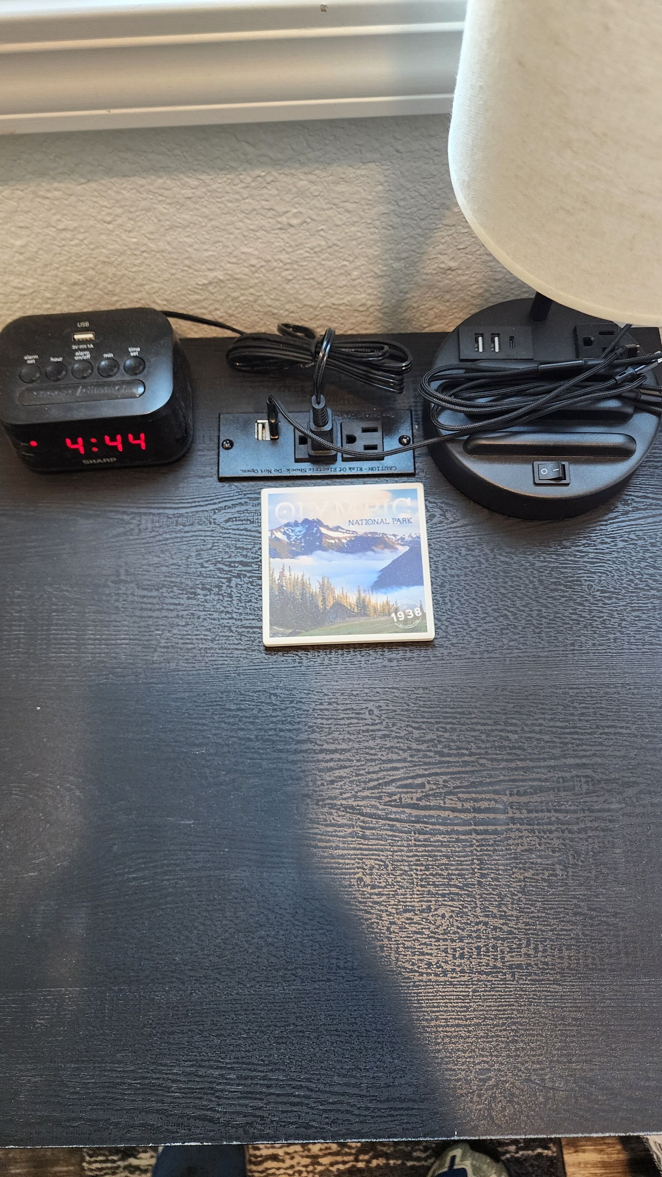Un escritorio con un cargador USB, un marco de fotos y una lámpara.