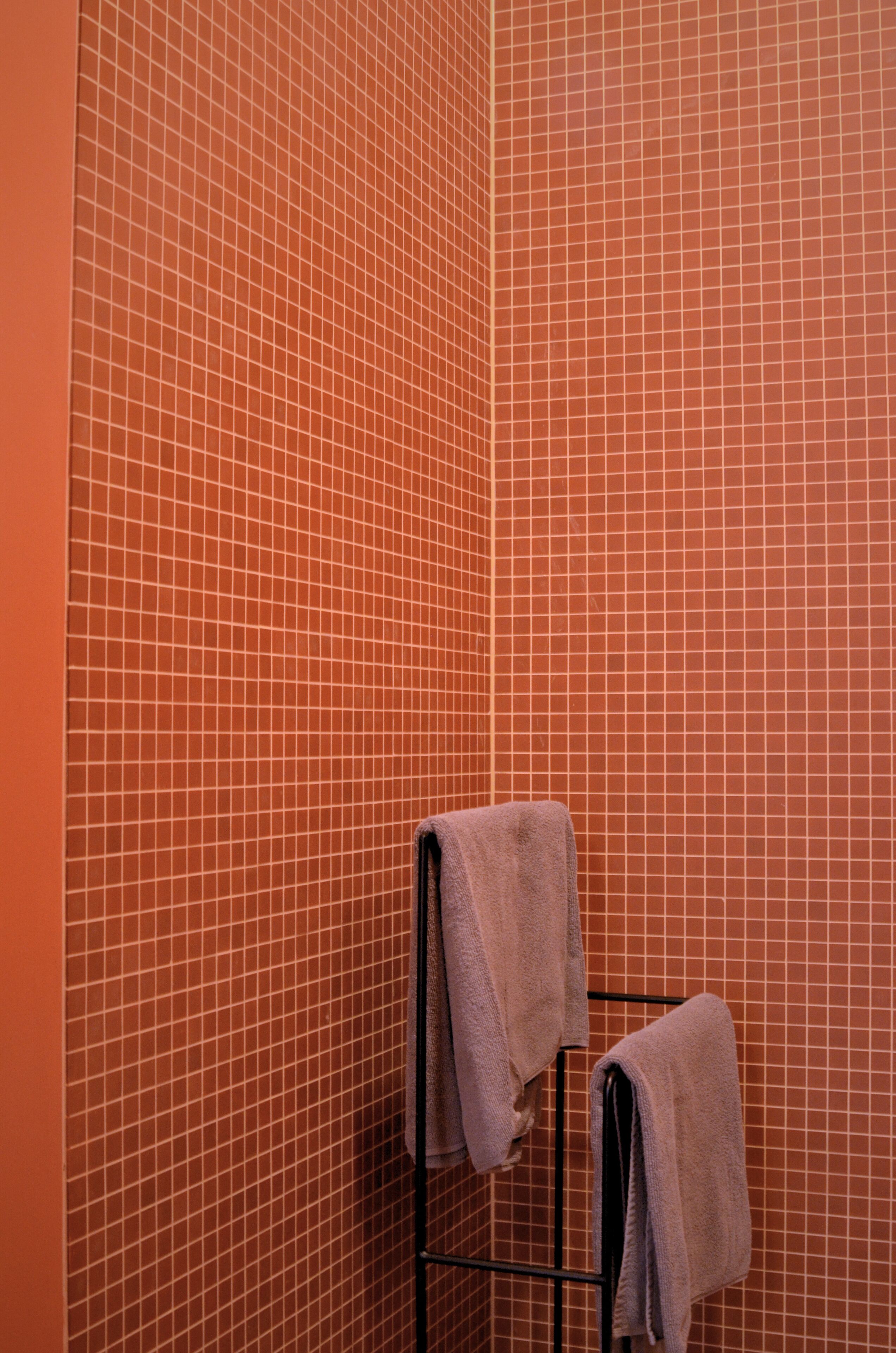 A bathroom with a tiled wall and a metal towel rack holding two towels.