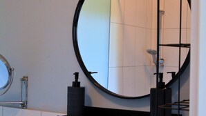 Een badkamer met een ronde spiegel, een handdoekrek en een zeepdispenser op een plank.