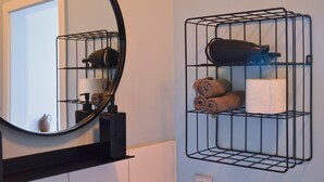 Een badkamer met een ronde spiegel, een zwarte handdoekhouder en een zwart metalen plankje met handdoeken en toiletartikelen.